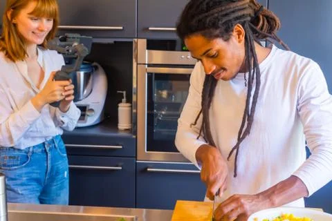 Black guy cutting food while a girl records it with a mobile Stock Photos