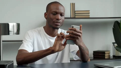 Black guy at the desk in the office is smiling happily, holding a smartphone in Stock Footage 168742101