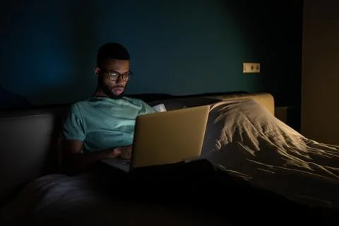 Black guy freelance IT developer using laptop at night, coding until late hours 库存照片