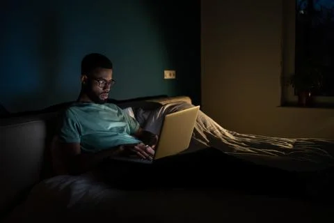 Black guy freelance IT developer using laptop at night, coding until late hours Foto stock