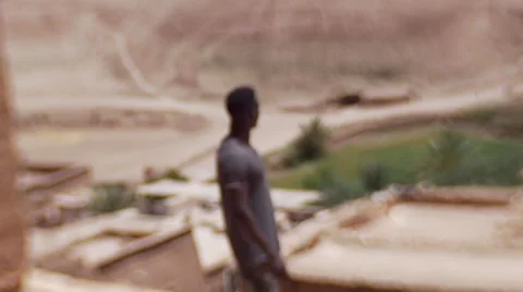 Black guy on a high peek of sand houses and looks around at the desert 05 Stock Footage 67531996
