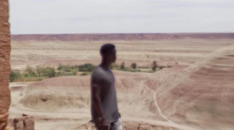 Black guy on a high peek of sand houses and looks around at the desert 04 Видео 67532010