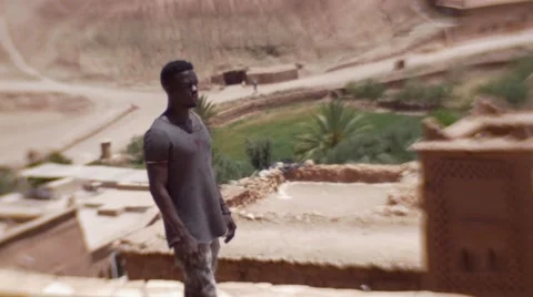 Black guy on a high peek of sand houses and looks around at the desert 03 Video stock 67532023