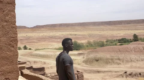 Black guy on a high peek of sand houses and looks around at the desert 02 Stock Footage 67557965