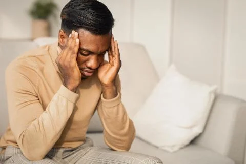 Black Guy Suffering Having Headache Sitting On Couch At Home Фото