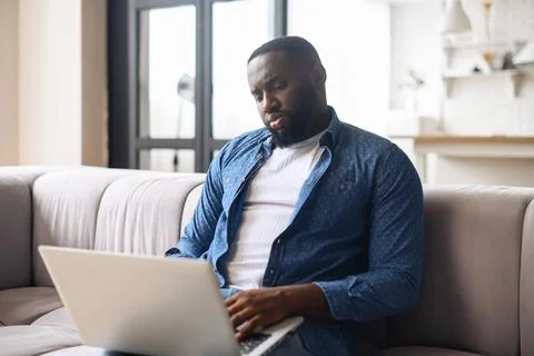 Black guy using laptop sitting on the couch Stock Photos