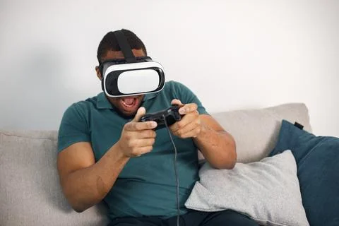 Black guy with virtual reality glasses sitting on a couch in living room Stock Photos