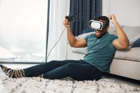 Black guy with virtual reality glasses sitting on a carpet in living room Stock Photos