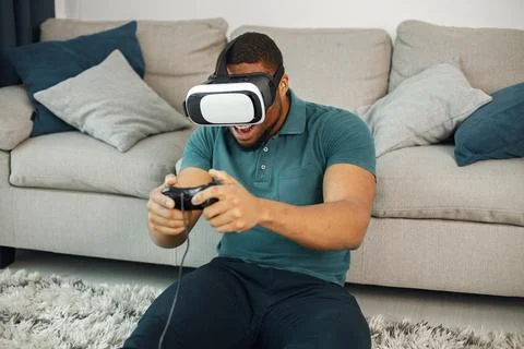 Black guy with virtual reality glasses sitting on a carpet in living room Stock Photos