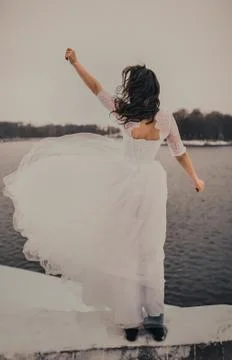 Black-haired bride in a white wedding dress stands above the river Stock Photos