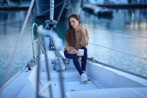 Black-haired girl on a yacht with a hot drink jeans, white boots Stock Photos