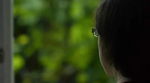 Black-haired woman looks out the window in the yard with green vegetation 1 Stock Footage 59588308