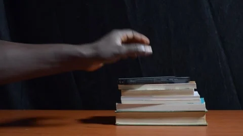 A black hand placing a phone on a stack of books on the table Stock Footage 276593690