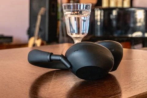 Black handheld electronic devices resting on a wooden table beside a glass .. 스톡 사진