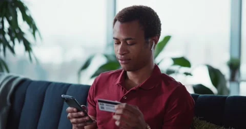 Black handsome guy using cellphone typing debit card number paying for online Stock Footage 148161338
