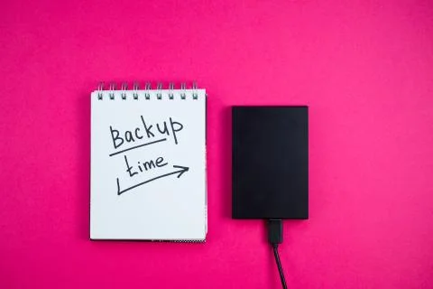 Black hard drive with a Notepad Backup text time is lying on a pink backgroun Stock Photos