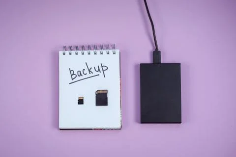 Black hard drive, notepad with backup text is lying on a lilac background. Stock Photos