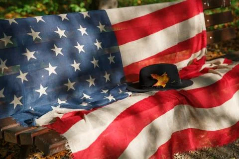 Black hat with a yellow maple leaf on a bench with an American flag Stock Photos