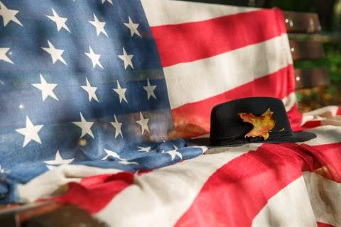 Black hat with a yellow maple leaf on a bench with an American flag Stock Photos