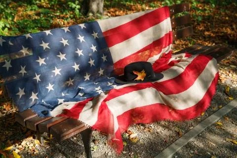 Black hat with a yellow maple leaf on a bench with an American flag Stock Photos