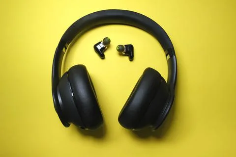 Black headphone and tiny earbuds on yellow background Foto stock