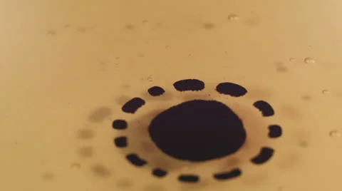 Black ink particles expanding circular on yellow liquid Video stock 59657799