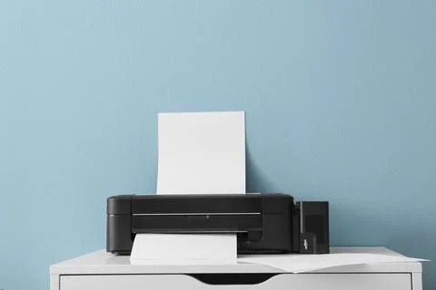 Black inkjet printer with blank paper sheets on white desk against blue wall, Stockfoto's