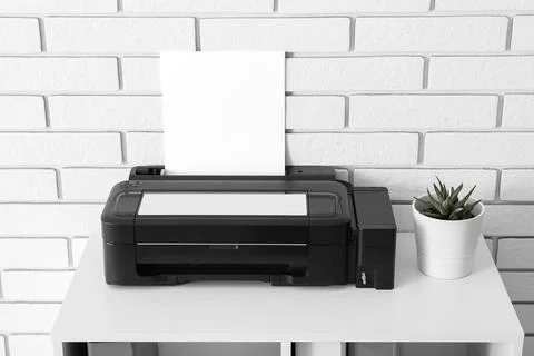 Black inkjet printer with blank paper on a white desk against a white brick w Stock Photos