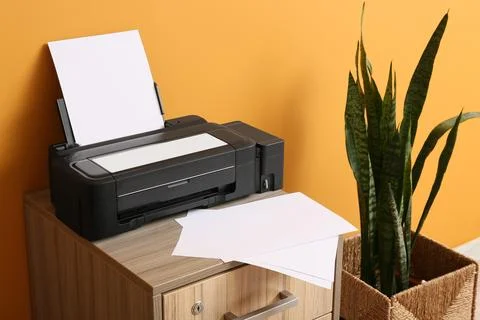 Black inkjet printer with blank white paper on a wooden cabinet next to a sna Stock Photos