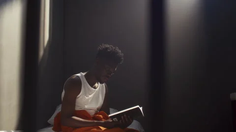 Black Inmate Reading Book while Sitting on Prison Bed Stock Footage 311608777