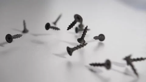 Black iron screws fall onto a white table and crumble bouncing in slow motion Stock Footage 131563495