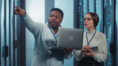 Black IT administrator instructing young female intern showing multiple rack Stock Footage 119782379