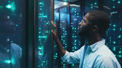 Black IT system administrator visually inspecting typing on high tech server Stock Footage