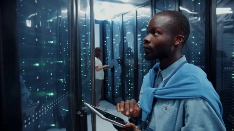 Black IT tech professional running backups on digital tablet wirelessly managing Stock-Footage 121223786