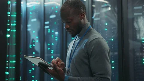 Black IT tech specialist checking hardware in rack server cabinets. Bearded Stock Footage 119784165