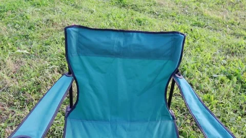 A black jacket falls on the back of a green chair against a background of grass Vídeo Stock 139049229