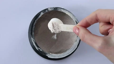 Black jar with electrolytes in measuring spoon in woman's hand on white Vidéo 234985571
