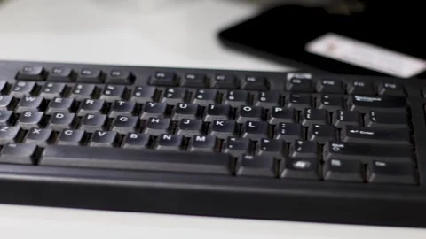 A black keyboard connected to a computer sits on an office desk. Stock Footage 299673799