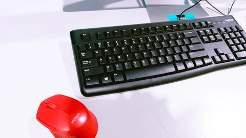 A black keyboard with a red mouse placed on a desk. Stock Photos
