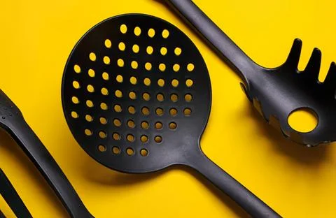 Black kitchen spaghetti strainer and tongs on yellow background Stock Photos
