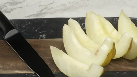 A black knife is skillfully slicing fresh melon on a wooden board, displaying Видео 279835736