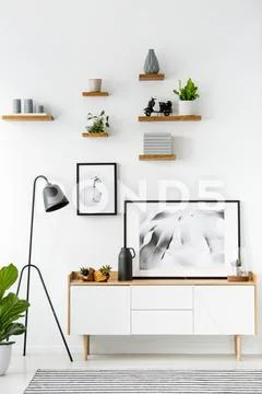 Black lamp next to cupboard against white wall with posters in simple flat in Stock Photos