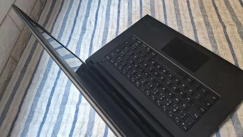 Black laptop computer resting open on a blue striped fabric surface Stock Photos