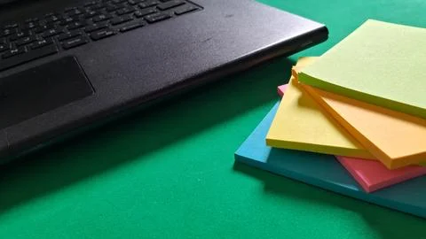 Black laptop computer sitting next to colorful sticky note pads Stock Photos