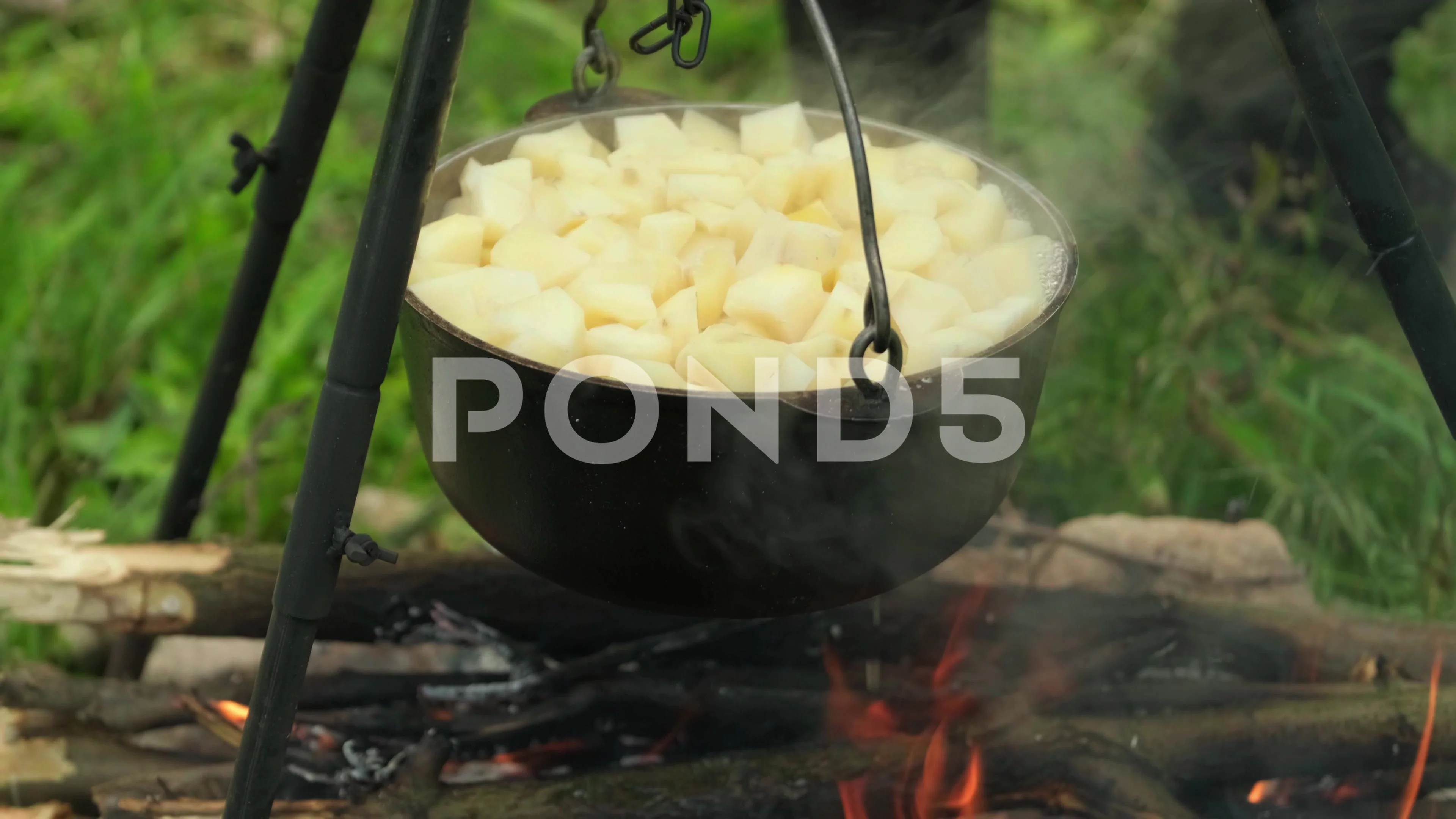 Black large tourist pot hangs over burning flame of campfire in the forest.  Cooking dinner on