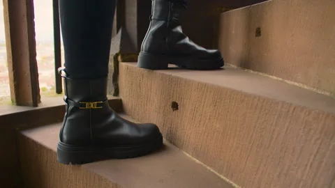 Black leather boots step up the worn-out stone stairs inside a cathedral Stock Footage 315243429