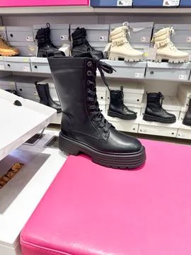 Black leather combat boot displayed on a bright pink bench in a shoe store... Stock Photos