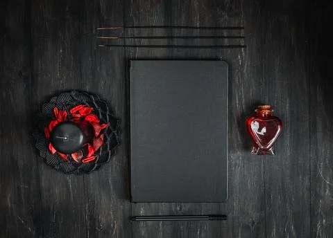 A black leather empty book, a candle in a metal saucer with a dried flower, r Stock Photos