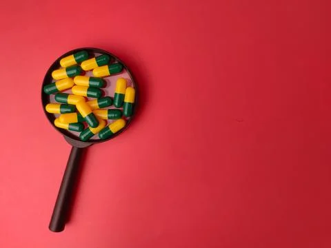 A black magnifying glass frames a cluster of green and yellow medicine caps.. Stock Photos