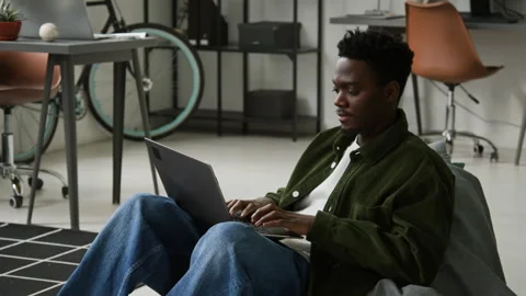 Black Male Programmer Writing Code on Laptop Sitting in Bean Bag Chair Stockbeeldmateriaal 335939608